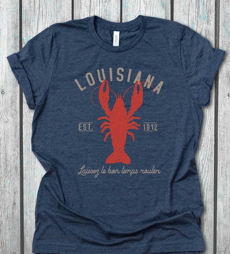 Op de afbeelding: Een marineblauw t-shirt met een vintage-stijl afbeelding van een rode rivierkreeft en de tekst "Louisiana Est. 1812" en "Laissez le bon temps rouler".