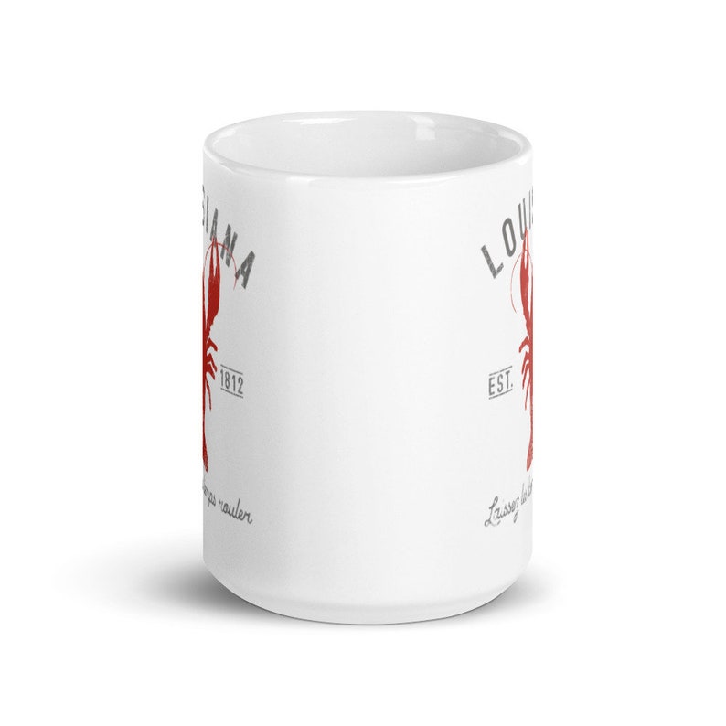 May include: A white ceramic mug featuring a red crawfish graphic, the text LOUISIANA, the year 1812, and the phrase Laissez les bons temps rouler in grey lettering. The design is printed on the side of the cylindrical mug with a handle.