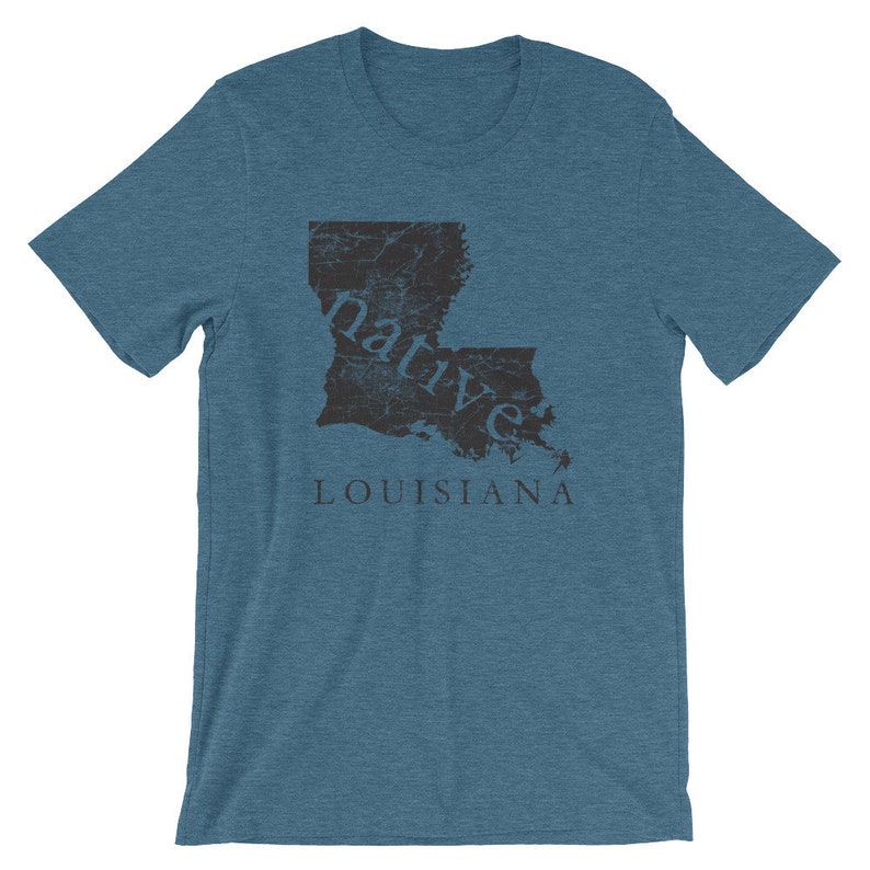 May include: A heathered blue short-sleeve t-shirt featuring a dark gray graphic of the state of Louisiana. The word native is printed in lowercase letters across the state shape, with the word LOUISIANA printed in capital letters below it.