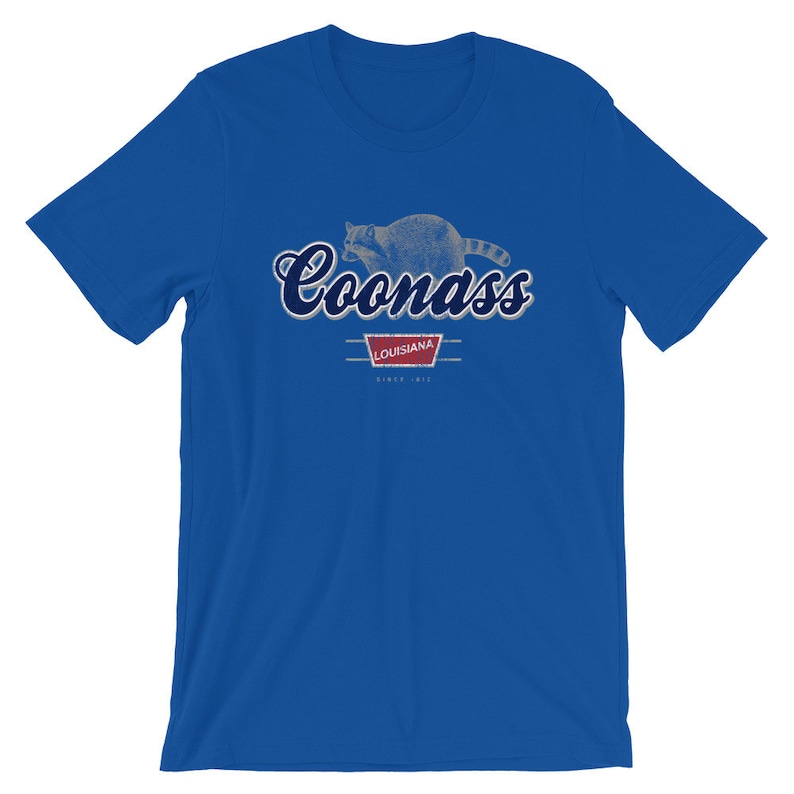 May include: A royal blue t-shirt with a distressed graphic of a raccoon and the text "Coonass Louisiana Since 1912".