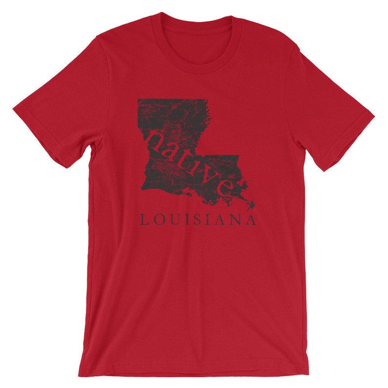 May include: A red short-sleeved t-shirt featuring a black graphic of the state of Louisiana. The word native is printed in red across the center of the state map, and the word LOUISIANA is printed in black capital letters below the map graphic.