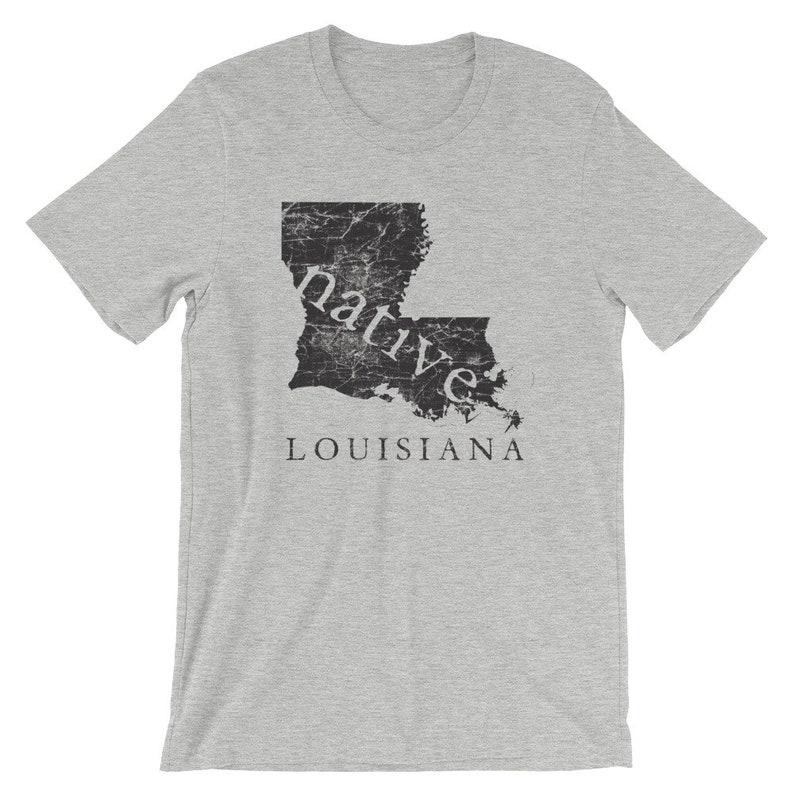 May include: A heather grey short-sleeve t-shirt featuring a black, distressed-texture graphic of the state of Louisiana. The word "native" is printed in white lowercase letters across the map, with the word "LOUISIANA" in black below it.