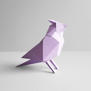 Può includere: Un uccello di origami lavanda con un design geometrico. L'uccello è fatto di carta e ha una coda lunga e un becco appuntito.
