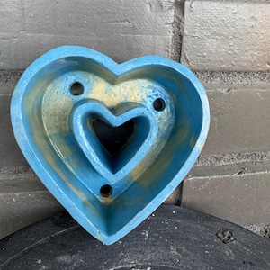 May include: A blue and yellow heart-shaped planter with two holes on the top and one on the bottom. The planter has a smaller heart-shaped cutout inside.