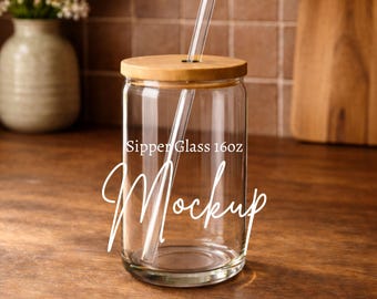 May include: A clear glass sipper cup with a wooden lid and a clear straw. The cup has the words "Sipper Glass 16oz" and "Mockup" printed on it. The cup is sitting on a wooden surface.