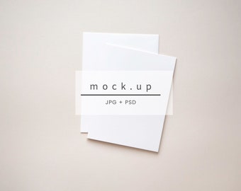 May include: Two white blank cards stacked on top of each other on a light beige background. The text "mock.up" and "JPG + PSD" is printed in black on the top card.