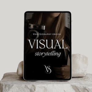 Op de afbeelding: Een zwart-witte digitale tablet met de tekst "PHOTOGRAPHY EBOOK VISUAL storytelling" en een logo van een gestileerde "V" op een zwarte achtergrond. De tablet ligt op een lichtgrijze stenen ondergrond.