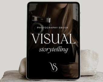 May include: A black and white digital tablet with the text "PHOTOGRAPHY EBOOK VISUAL storytelling" and a logo of a stylized "V" on a black background. The tablet is sitting on a light gray stone surface.