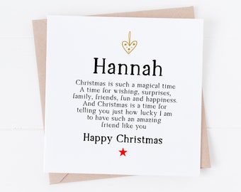 Può includere: Biglietto di Natale bianco con il nome "Hannah" in grassetto. Presenta un cuore dorato e il testo "Happy Christmas" con una stella rossa. Il biglietto è su una busta marrone, con un messaggio sull'amicizia.