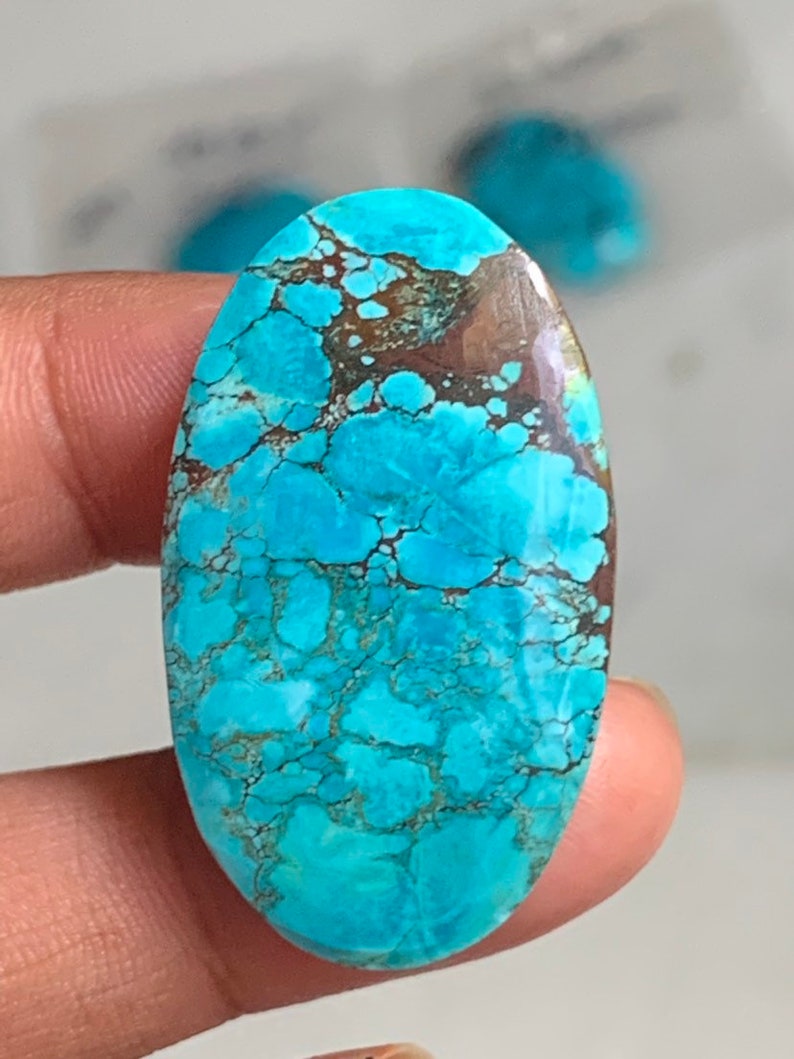 May include: Oval turquoise gemstone with brown veining. The stone's surface is a vibrant, mottled blue, showcasing natural patterns. This polished gemstone is ideal for jewelry making or collecting.