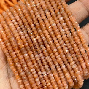 May include: A strand of peach-colored sunstone beads. The beads are faceted and have a shimmery, iridescent quality. The beads are strung on a clear thread and are ready to be used for jewelry making.