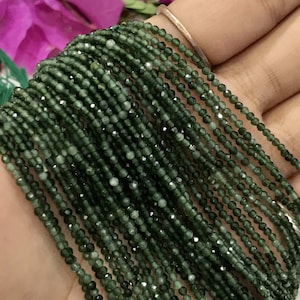K&ouml;nnte beinhalten: Eine Str&auml;hne dunkelgr&uuml;ner Edelsteinperlen mit einem Durchmesser von etwa 2 mm und einer facettierten Oberfl&auml;che. Die Perlen sind auf einem durchsichtigen Faden aufgef&auml;delt und in einer geraden Linie angeordnet.
