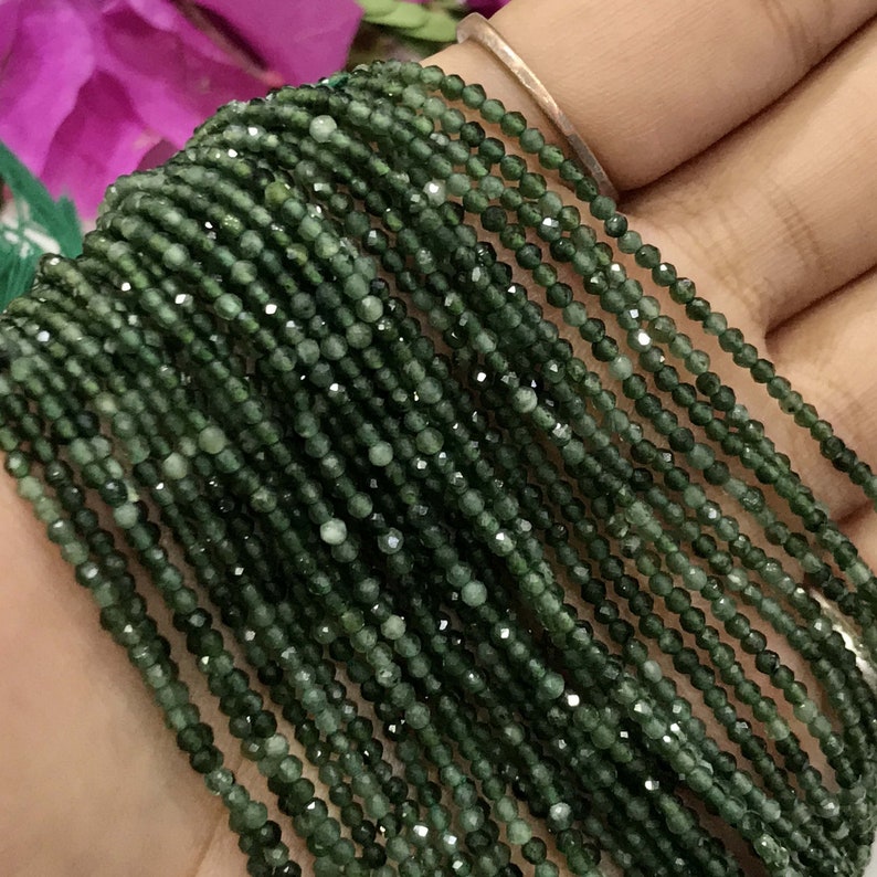 K&ouml;nnte beinhalten: Eine Str&auml;hne dunkelgr&uuml;ner Edelsteinperlen mit einem Durchmesser von etwa 2 mm und einer facettierten Oberfl&auml;che. Die Perlen sind auf einem durchsichtigen Faden aufgef&auml;delt und in einer geraden Linie angeordnet.