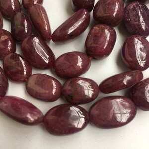 May include: A strand of deep red ruby gemstone beads, each bead is oval shaped and polished to a smooth, glossy finish.