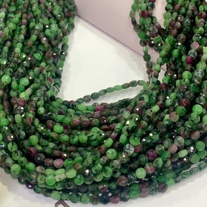 May include: Strands of faceted gemstone beads in shades of green and burgundy. The beads are small and round, with a polished, reflective surface. The gemstones are strung together, creating a cascading effect. The overall theme is jewelry.
