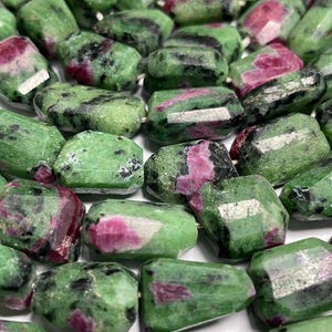 Puede incluir: Hilo de cuentas de piedras preciosas de rubí zoisita verdes y rosas. Las cuentas son rectangulares con bordes facetados. El color verde está moteado de negro y el color rosa está en parches. Las cuentas están ensartadas en un hilo blanco.