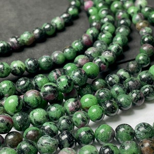 May include: Strands of round beads in shades of green, black, and maroon. The beads have a polished, glossy finish. The beads are likely for jewelry making or crafting.