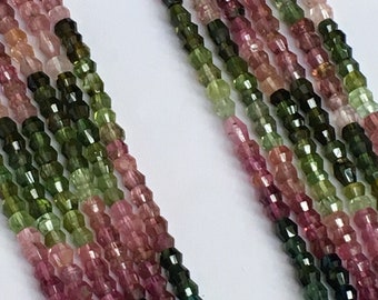 Pode incluir: Close-up de fios de contas de turmalina facetadas em tons de rosa, verde e castanho. As contas são enfiadas, criando uma exibição texturizada e colorida. As pedras preciosas são dispostas sobre um fundo branco.