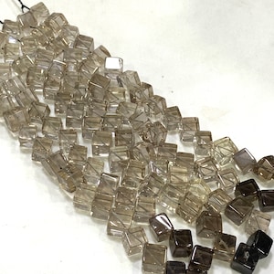 Puede incluir: Una hebra de cuentas de cuarzo ahumado, con cuentas facetadas de forma cuadrada en varios tonos de marrón y transparente. Las cuentas están enhebradas en un hilo transparente y están listas para la elaboración de joyas.