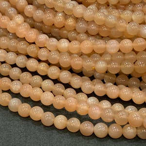 May include: A strand of peach-colored sunstone beads. The beads are round and smooth, with a slight shimmer.