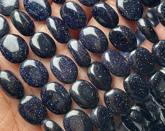 May include: A strand of polished, oval-shaped blue sandstone beads. The beads have a dark blue base color with sparkling inclusions, giving them a starry appearance. The beads are strung together, ready for jewelry making.