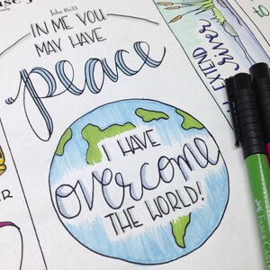 May include: A hand-drawn illustration of a globe with the words "I have overcome the world!" written in blue cursive. The globe is surrounded by a white background with the words "In me you may have peace" written in black cursive above the globe. The words "John 16:33" are written in black cursive above the words "In me you may have peace".