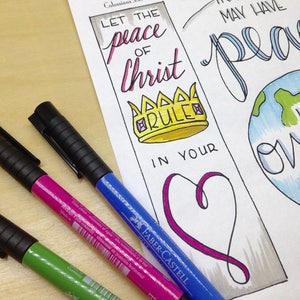May include: A white paper bookmark with a hand-drawn illustration of a crown, a heart, and a globe. The bookmark features the text "Let the peace of Christ rule in your heart" and "I have overcome the world".