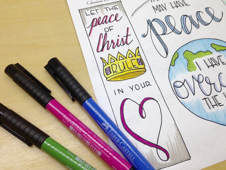 May include: A white paper bookmark with a hand-drawn illustration of a crown, a heart, and a globe. The bookmark features the text "Let the peace of Christ rule in your heart" and "I have overcome the world".