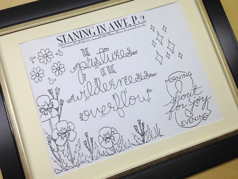 May include: Framed art print with black ink illustrations and handwritten text. The artwork includes floral and diamond shapes, and the words "STANING IN AWE P.2" and "THE pastures of the wilderness overflow". The frame is black with a gold inner border.