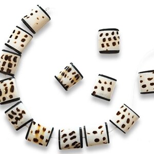 May include: A strand of white and brown shell beads with black trim. The beads are square shaped and have a mottled pattern. There are also several loose beads in the image.