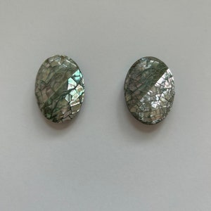 May include: A pair of oval earrings with a mosaic pattern. The earrings have a shimmering, iridescent appearance, with green, silver, and blue hues. The surface has a cracked effect, giving them a distinctive texture.
