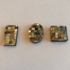 Könnte beinhalten: Drei dekorative Mosaikfliesen in verschiedenen Formen: ein Rechteck, ein Oval und ein Quadrat. Die Fliesen sind aus irisierendem Perlmutt und haben einen schwarzen Hintergrund.