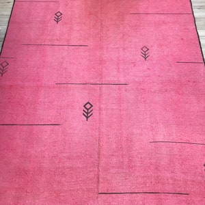 K&ouml;nnte beinhalten: Ein rosa Teppich mit einem geometrischen Muster aus schwarzen Linien und Diamanten. Der Teppich hat einen subtilen Ombre-Effekt, der von einem dunkleren Rosa oben zu einem helleren Rosa unten verblasst.