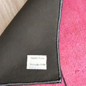 K&ouml;nnte beinhalten: Nahaufnahme der R&uuml;ckseite eines rosafarbenen Teppichs mit einem schwarz-wei&szlig;en Rand. Der Teppich hat ein Etikett mit der Aufschrift "KENDIR KILIM 160 x 230 = 3,67 m 7,9' x 9,5' feet".