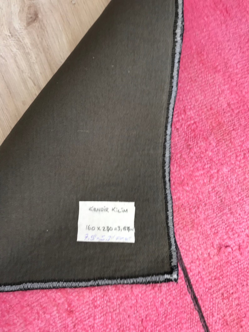 K&ouml;nnte beinhalten: Nahaufnahme der R&uuml;ckseite eines rosafarbenen Teppichs mit einem schwarz-wei&szlig;en Rand. Der Teppich hat ein Etikett mit der Aufschrift "KENDIR KILIM 160 x 230 = 3,67 m 7,9' x 9,5' feet".