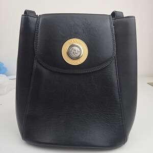 Pu&ograve; includere: Borsa a tracolla in pelle nera con chiusura a patta. La borsa presenta un emblema circolare dorato con la scritta "GIANNI VERSACE" e una testa di Medusa. La borsa ha una forma strutturata e un manico superiore.