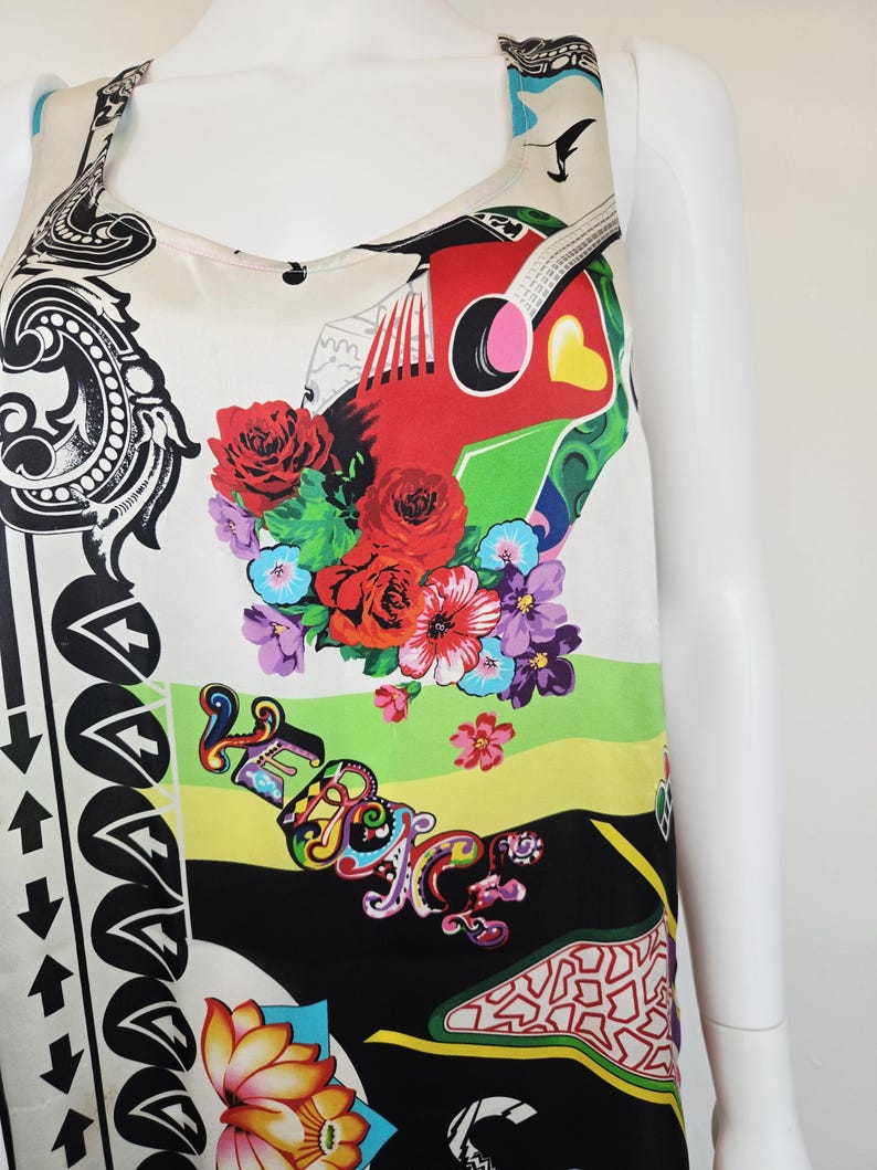 Puede incluir: Una blusa sin mangas con un estampado gr&aacute;fico vibrante y multicolor sobre un fondo crema. El dise&ntilde;o incluye rosas rojas, una guitarra estilizada, motivos florales y la palabra VERSACE en letras decorativas coloridas, junto a patrones de flechas negras.