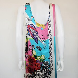 Puede incluir: Un vestido sin mangas con un estampado gr&aacute;fico multicolor y vibrante sobre un fondo claro. El dise&ntilde;o incluye una guitarra el&eacute;ctrica estilizada, rosas rojas y negras, y notas musicales. La palabra VERSACE est&aacute; impresa cerca del dobladillo.