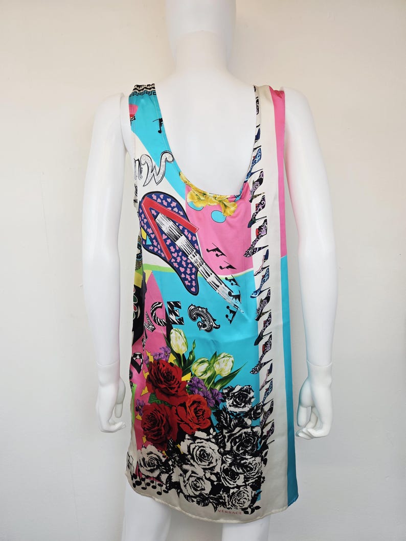 Puede incluir: Un vestido sin mangas con un estampado gr&aacute;fico multicolor y vibrante sobre un fondo claro. El dise&ntilde;o incluye una guitarra el&eacute;ctrica estilizada, rosas rojas y negras, y notas musicales. La palabra VERSACE est&aacute; impresa cerca del dobladillo.