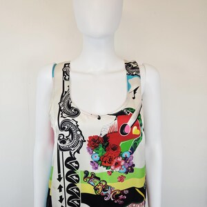 Puede incluir: Una camiseta sin mangas con base color crema y un estampado gr&aacute;fico vibrante. El dise&ntilde;o incluye una guitarra roja, arreglos florales coloridos, bordes con volutas negras y la palabra Versace en letras estilizadas sobre una franja verde brillante.