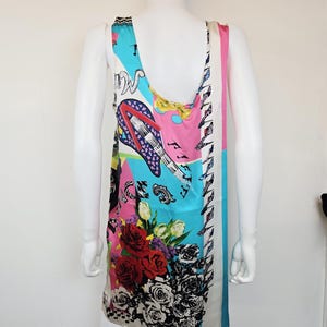 Puede incluir: Un vestido sin mangas con un estampado gr&aacute;fico multicolor y vibrante. El dise&ntilde;o incluye una guitarra el&eacute;ctrica estilizada, notas musicales y grandes arreglos florales con rosas rojas y negras. El logotipo de Versace es visible en el dobladillo.