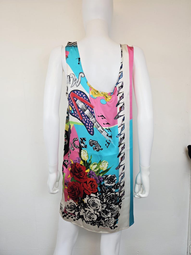 Puede incluir: Un vestido sin mangas con un estampado gr&aacute;fico multicolor y vibrante. El dise&ntilde;o incluye una guitarra el&eacute;ctrica estilizada, notas musicales y grandes arreglos florales con rosas rojas y negras. El logotipo de Versace es visible en el dobladillo.