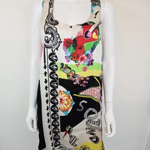 Puede incluir: Un vestido sin mangas de color crema con un estampado gr&aacute;fico vibrante. El dise&ntilde;o incluye una guitarra roja, flores coloridas, un zapato de tac&oacute;n, notas musicales y el texto "VERSACE" y "SOUND" en letras estilizadas sobre paneles negros y amarillos.