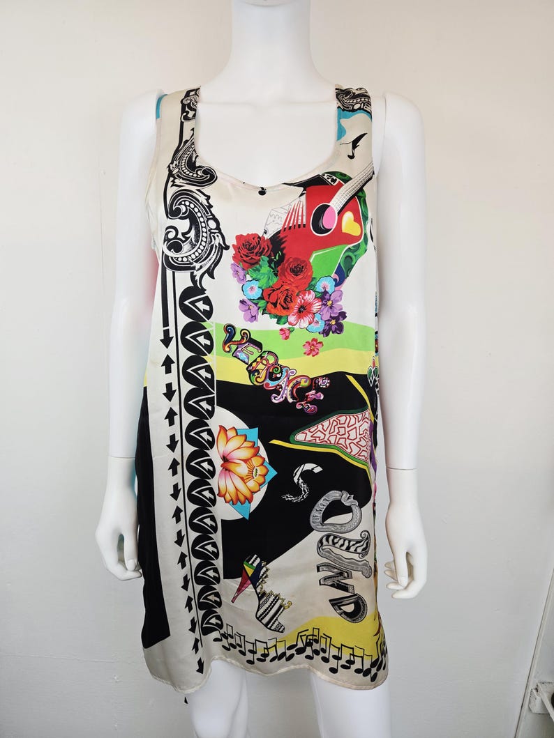 Puede incluir: Un vestido sin mangas de color crema con un estampado gr&aacute;fico vibrante. El dise&ntilde;o incluye una guitarra roja, flores coloridas, un zapato de tac&oacute;n, notas musicales y el texto "VERSACE" y "SOUND" en letras estilizadas sobre paneles negros y amarillos.