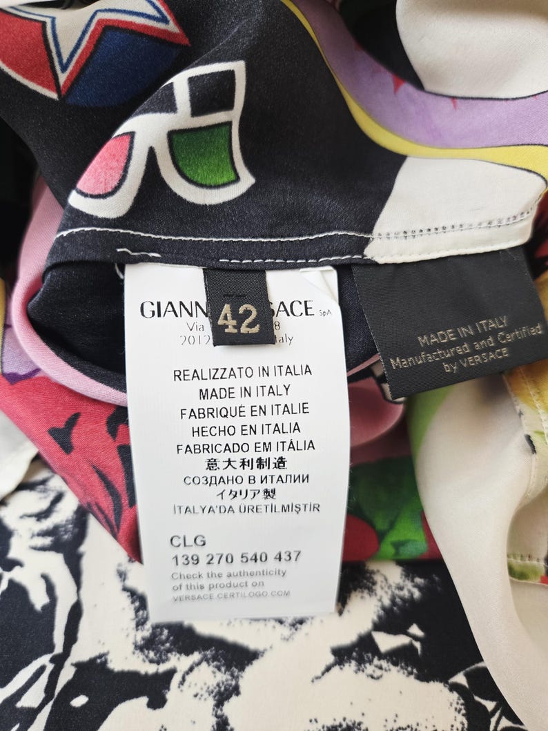 Puede incluir: Una prenda de seda multicolor con un estampado gr&aacute;fico llamativo de estrellas y formas abstractas. Incluye una etiqueta blanca con el texto GIANNI VERSACE, talla 42, MADE IN ITALY y el c&oacute;digo de autenticaci&oacute;n CLG 139 270 540 437.