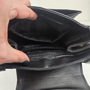 Pu&ograve; includere: Borsa a mano in pelle nera con interno aperto. La fodera interna presenta un motivo ripetuto del nome del marchio. La borsa ha una chiusura con patta e una piccola tasca. La borsa &egrave; progettata con uno stile classico ed elegante.