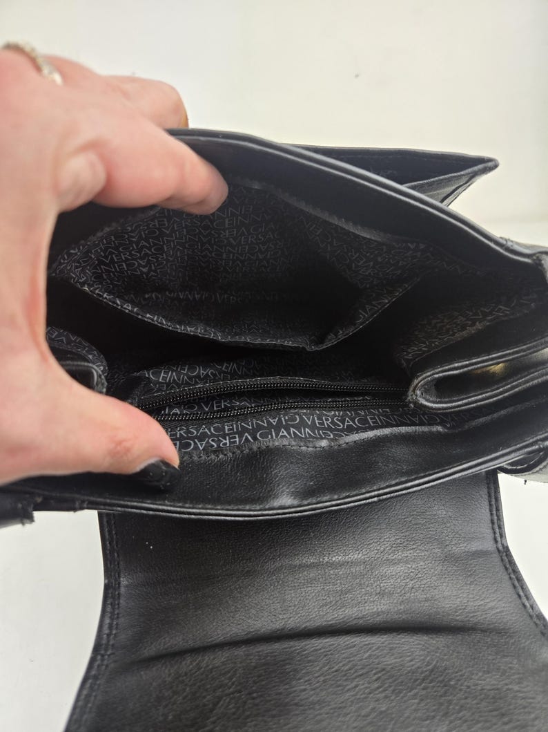 Pu&ograve; includere: Borsa a mano in pelle nera con interno aperto. La fodera interna presenta un motivo ripetuto del nome del marchio. La borsa ha una chiusura con patta e una piccola tasca. La borsa &egrave; progettata con uno stile classico ed elegante.