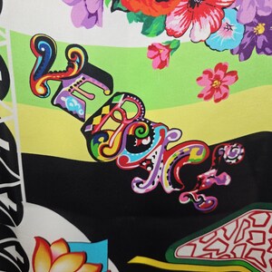 Puede incluir: Una tela con un estampado floral vibrante que presenta rosas rojas, flores moradas y azules, y hojas verdes. La palabra VERSACE est&aacute; impresa en una fuente estilizada y multicolor sobre un fondo de rayas horizontales verde lima, amarillo y negro.