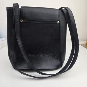 Pu&ograve; includere: Borsa a tracolla in pelle nera con chiusura a patta e lunghe cinghie. La borsa ha una forma rettangolare con una superficie strutturata e dettagli dorati. Le cinghie sono sottili e sembrano essere realizzate nello stesso materiale della borsa.