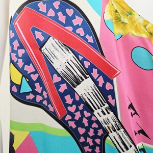 Puede incluir: Una prenda sin mangas con un estampado gr&aacute;fico vibrante y multicolor. El dise&ntilde;o incluye una letra A roja grande y estilizada sobre un fondo azul oscuro lleno de peque&ntilde;os corazones y flechas rosas, junto con motivos florales amarillos.